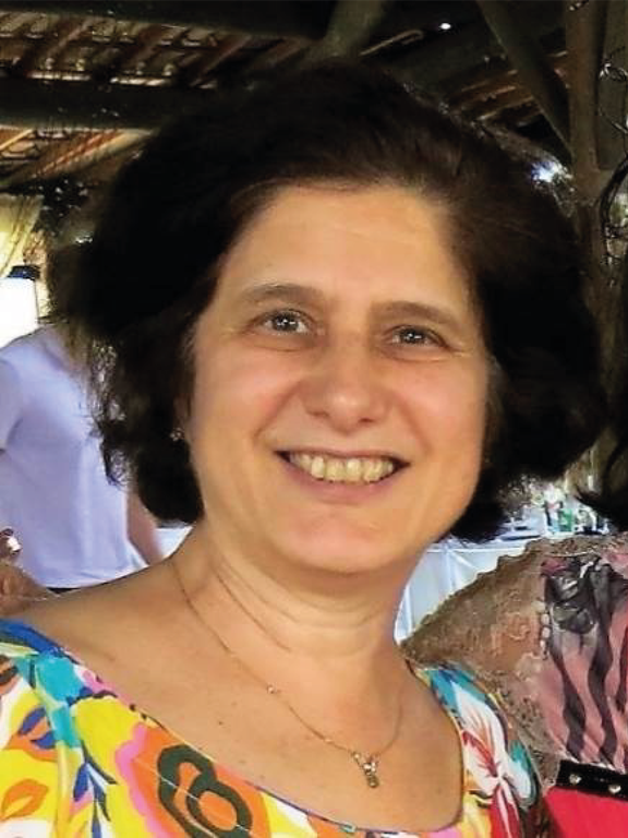 Woman, white, smiling, short brown hair, floral dress in yellow tones, thin little chain around her neck