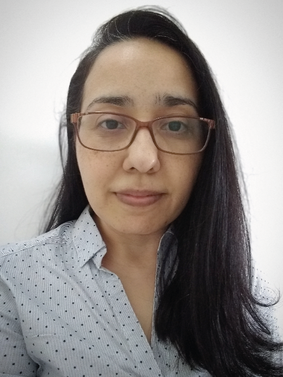 Woman, white, dark brown hair, long, wearing glasses with brown rectangular frame, light blue blouse with dark blue polka dots