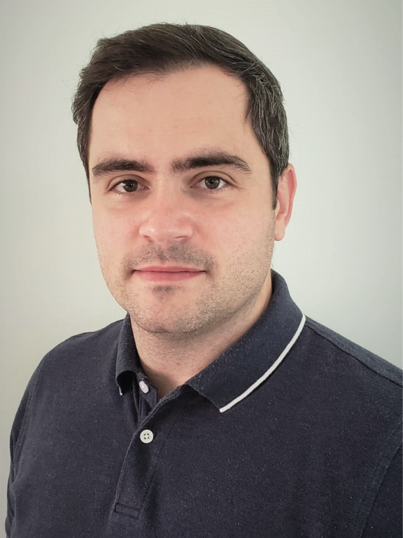 White man, with a short side parted black hair, brown eyes, thick eyebrows, wearing a dark blue polo shirt