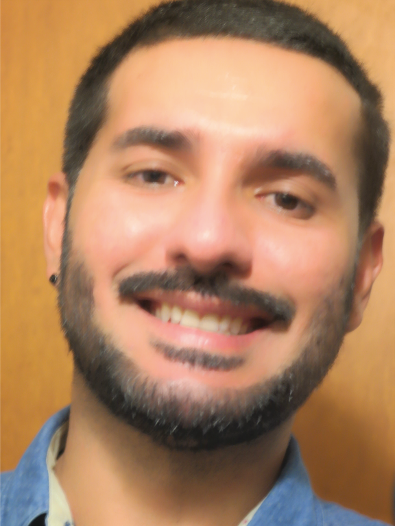 Mixed man with smile on his face, short and straight dark brown hair, using beard and wearing a blue shirt