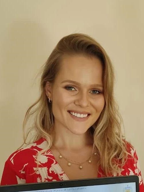 Docentes_Heloísa Bremm Madalosso.jpeg Woman, white, with blonde wavy hair, blue eyes, wearing a red and white floral dress.
