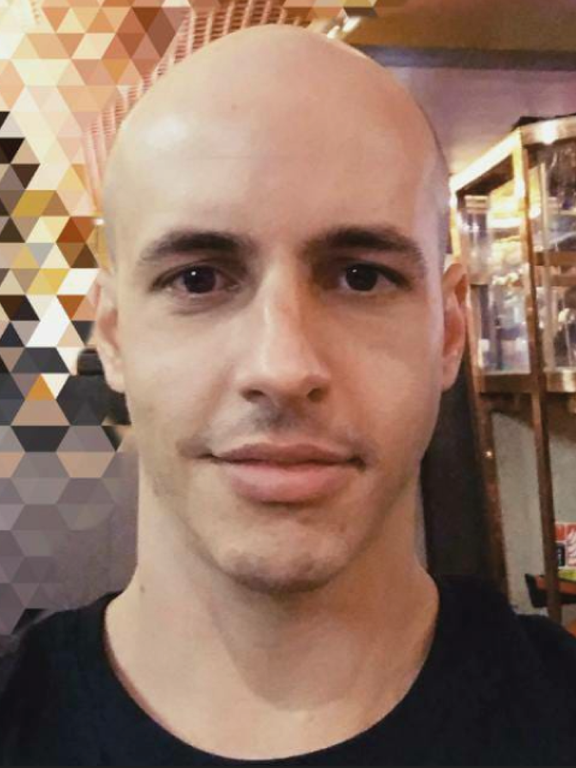 White, bald man, wearing a black t-shirt, with a mosaic in the background.