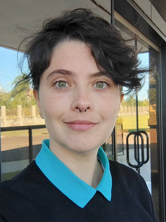 Tenho pele clara, olhos verdes e cabelo escuro e curto. Estou usando um moletom preto, com gola da camiseta polo turquesa à mostra.