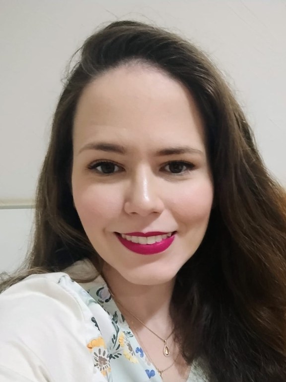 Mulher, branca, cabelos castanhos, longos e lisos, usando blusa branca.