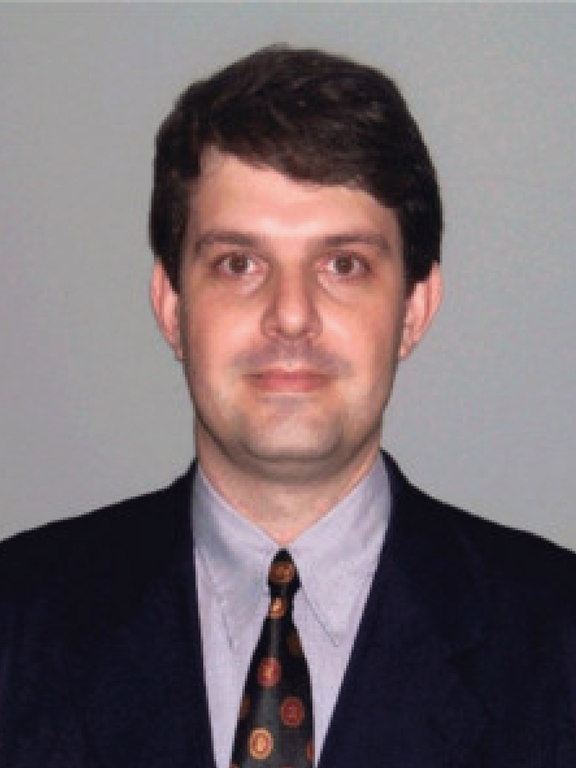 Homem branco, de cabelos escuros curtos usando óculos com armação quadrada